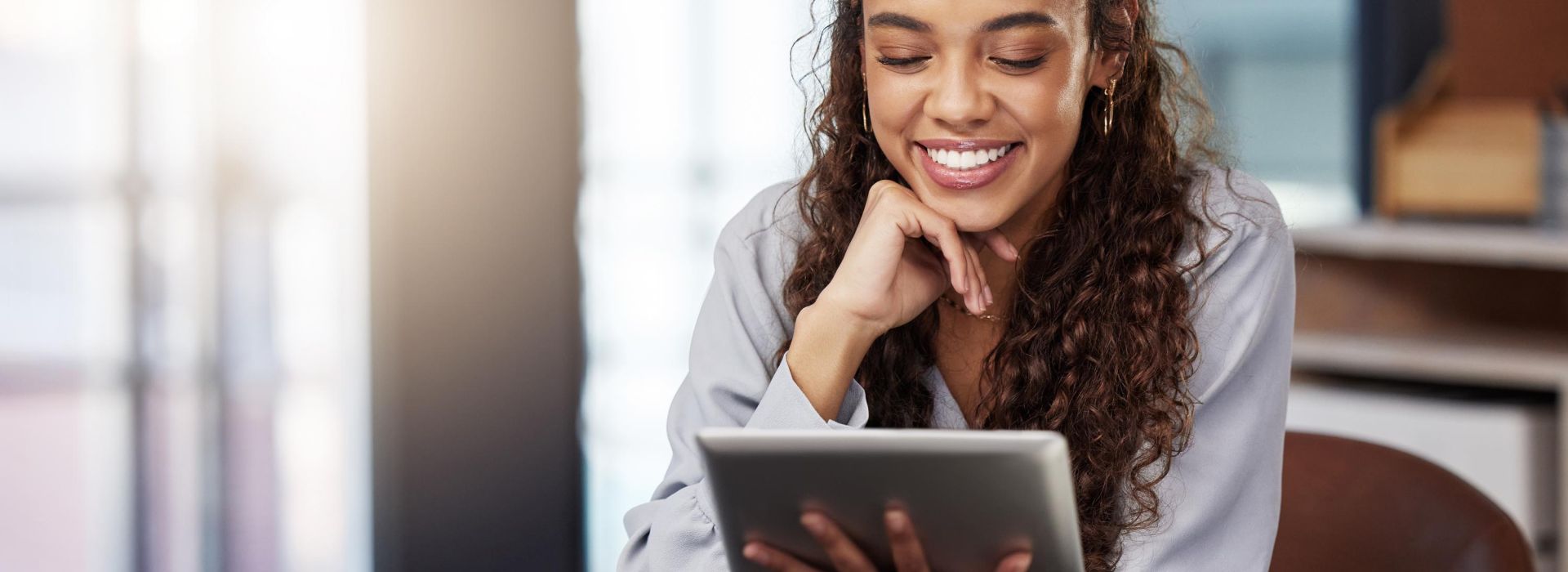 Happy woman at office desk looks at tablet held in her hand